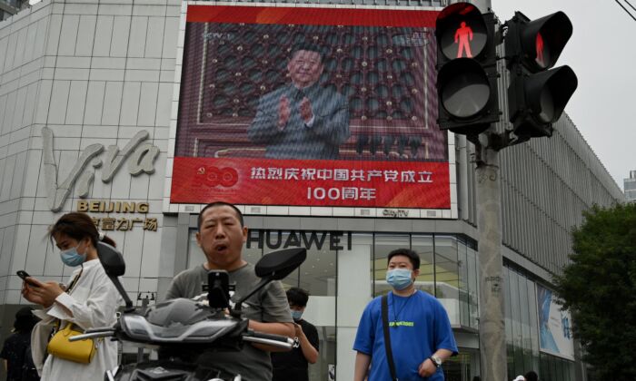 Unas personas caminan por delante de una gran pantalla que muestra al mandatario chino Xi Jinping dando un discurso durante las celebraciones para conmemorar el centenario de la fundación del Partido Comunista Chino en Beijing (China) el 1 de julio de 2021. (Noel Celis/AFP vía Getty Images)