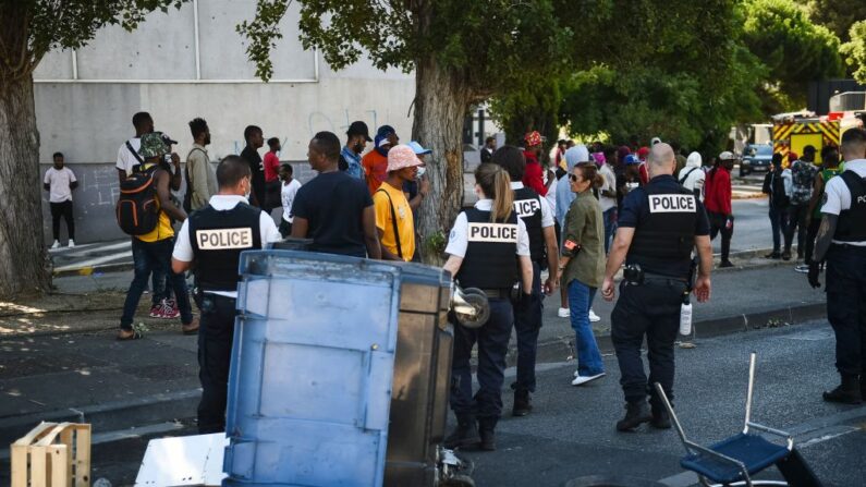 La gente se para en una calle mientras los agentes de policía tratan de asegurar el lugar donde tres personas perecieron en un incendio en un edificio parcialmente okupado, en 'Les Flamants', un barrio desfavorecido de Marsella, sur de Francia, el 17 de julio de 2021. (Clement Mahoudeau/AFP vía Getty Images)