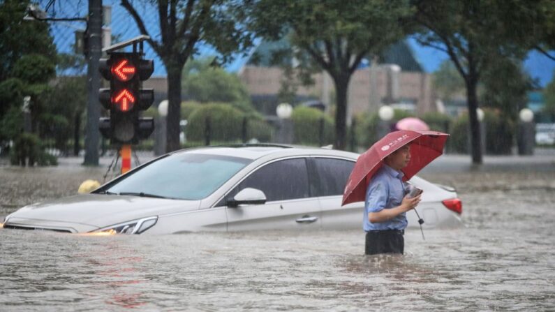 Un hombre pasa junto a un coche sumergido el 20 de julio de 2021, en una calle inundada en Zhengzhou, en la provincia central china de Henan. (STR/AFP vía Getty Images)