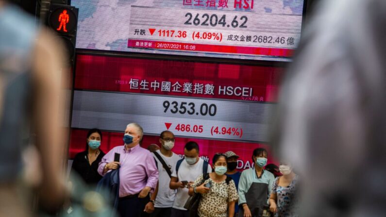 Un grupo de personas se encuentra frente a una pantalla electrónica que muestra el índice Hang Seng en el distrito central de Hong Kong el 26 de julio de 2021. (Isaac Lawrence/AFP vía Getty Images)