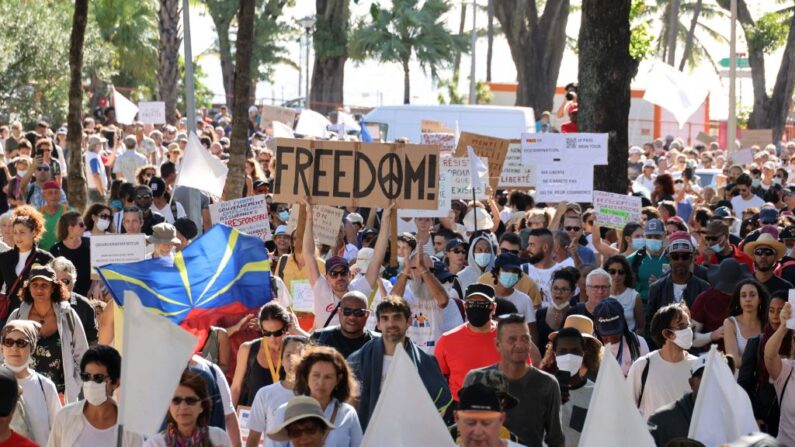Manifestantes sostienen pancartas y carteles, en uno de los cuales se lee "Libertad", durante una jornada nacional de protesta contra la vacunación obligatoria y el certificado sanitario en Saint-Denis de la Reunión, en la isla del Océano Índico, el 31 de julio de 2021. (Richard Bouhet/AFP vía Getty Images)