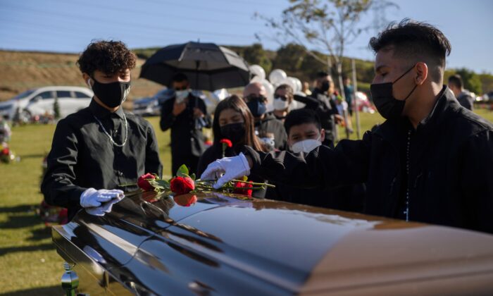 Gilberto Arias, de 15 años, (dcha.) y Javier Domínguez, de 13 años, colocan flores en el ataúd de Gilberto Arreguin Camacho, de 58 años, que murió a causa de la COVID-19, durante su entierro en un cementerio en Whittier (California) el 31 de diciembre de 2020. (Patrick T. Fallon/AFP vía Getty Images)