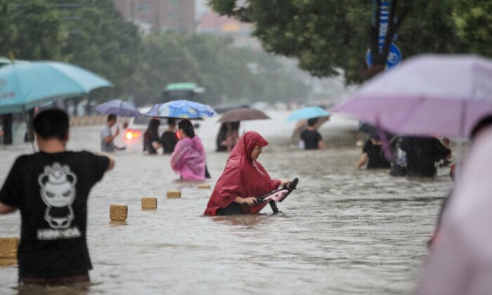 Varias personas atraviesan las aguas de una calle tras las fuertes lluvias en Zhengzhou, en la provincia central china de Henan, el 20 de julio de 2021. (STR/AFP vía Getty Images)