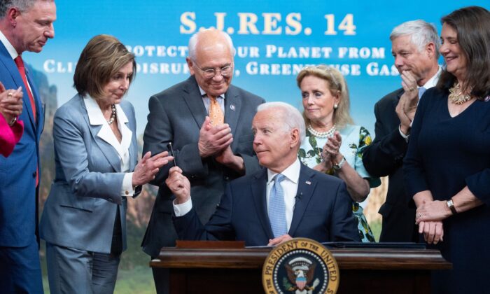El presidente Joe Biden entrega un bolígrafo a la presidenta Nancy Pelosi (2º Izq.), junto a otros miembros de la Cámara de Representantes, tras firmar un proyecto de ley sobre las emisiones de gases de efecto invernadero, en el Edificio de Oficinas Ejecutivas Eisenhower, en Washington, el 30 de junio de 2021. (Saul Loeb/AFP/Getty Images)