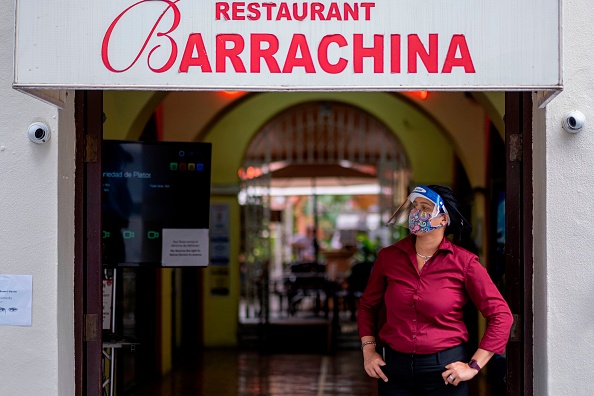 Una recepcionista de restaurante con una mascarilla y una careta protectora espera a los clientes en el Viejo San Juan, Puerto Rico, el 30 de junio de 2020, durante la pandemia de coronavirus. (Foto de RICARDO ARDUENGO/AFP a través de Getty Images)