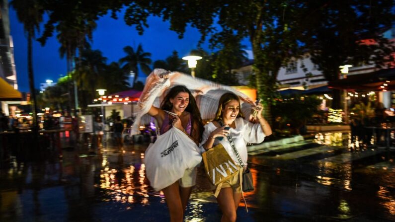 Mujeres se cubren de la lluvia con bolsas de la compra en Miami Beach, Florida (EE.UU.) el 27 de julio de 2021. (Chandan Khanna/AFP vía Getty Images)