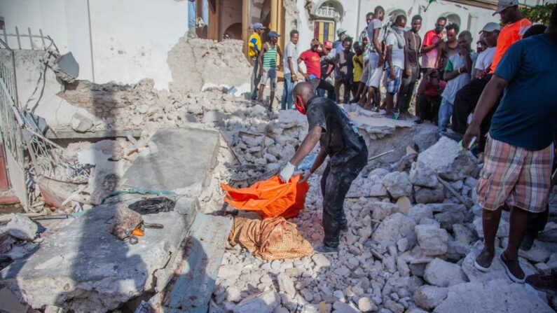 Unos haitianos observan una víctima del terremoto de 7.2 grados de magnitud el 15 de agosto de 2021 en Les Cayes, Haití. (Richard Pierrin/Getty Images)