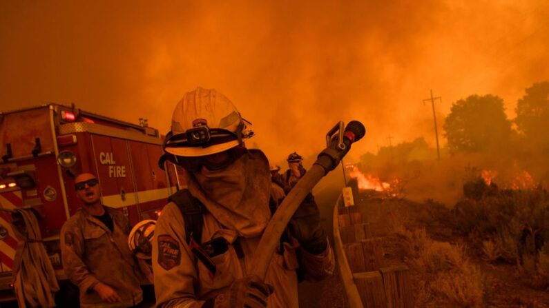 Los bomberos de Cal Fire colocan una línea de manguera mientras intentan contener el fuego del incendio Dixie Fire a través de la carretera 395, cerca de Milford, California, el 17 de agosto de 2021. (Patrick T. Fallon/AFP vía Getty Images)