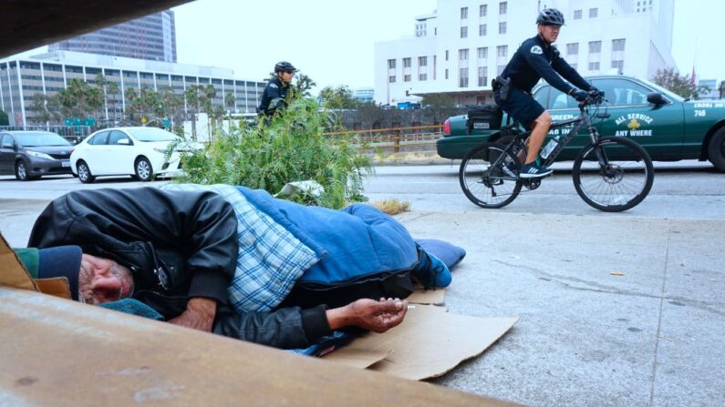Agentes del Departamento de Policía de Los Ángeles patrullan en bicicleta junto a un indigente en una acera del centro de la ciudad, en Los Ángeles, California, el 7 de junio de 2017. (FREDERIC J. BROWN/AFP/Getty Images)