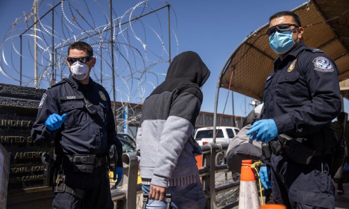 Solicitantes de asilo pasan entre los oficiales de Aduanas y Protección Fronteriza de EE.UU. mientras cruzan un puente de México hacía Estados Unidos, en Ciudad Juárez, México, el 17 de marzo de 2021. (John Moore/Getty Images)