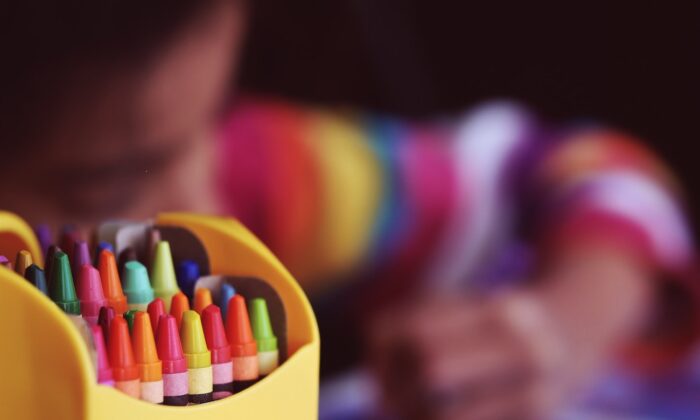 Foto de archivo de un niño sentado cerca de unos lápices de colores. (Aaron Burden/Unsplash)