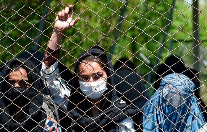 Una mujer con mascarilla se asoma desde una valla de hierro. (WAKIL KOHSAR/AFP vía Getty Images