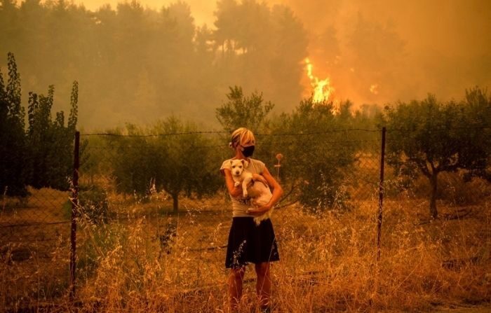 Una mujer sostiene un perro en sus brazos mientras los incendios forestales se acercan al pueblo de Pefki en la isla de Evia (Euboea), la segunda isla más grande de Grecia, el 8 de agosto de 2021. (ANGELOS TZORTZINIS/AFP vía Getty Images)