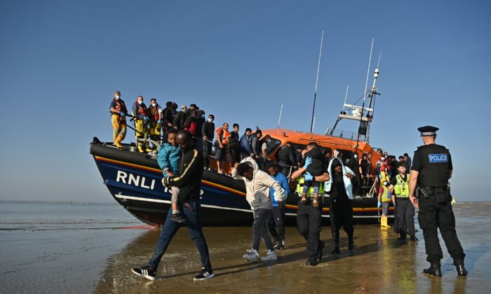 Inmigrantes ilegales llevan niños mientras son escoltados para ser procesados tras ser recogidos por un bote salvavidas de la Institución Real Nacional de Salvamento mientras cruzan el Canal de la Mancha en una playa de Dungeness, al sureste de Inglaterra, el 7 de septiembre de 2021. (Ben Stansall/AFP vía Getty Images)