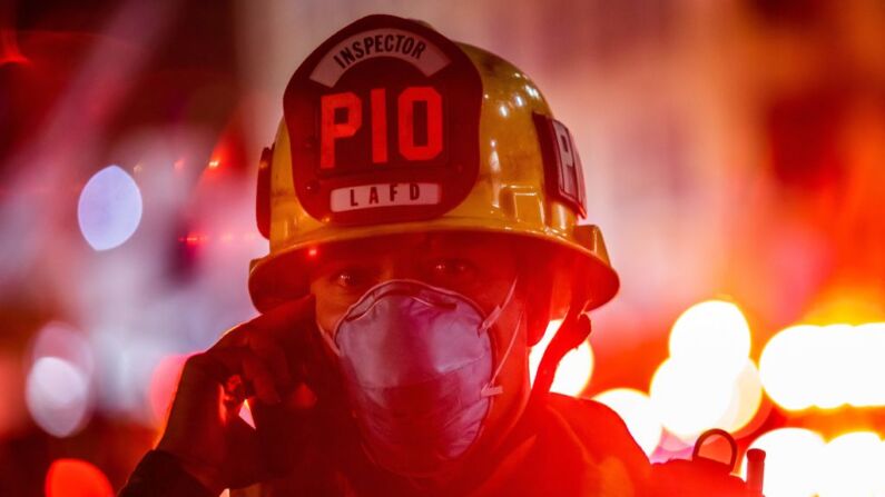 Un oficial de información pública del Departamento de Bomberos de Los Ángeles con una máscara facial habla por teléfono después de que un incendio en un edificio comercial que provocó una fuerte explosión en el Distrito Toy el 16 de mayo de 2020. (APU GOMES/AFP vía Getty Images)