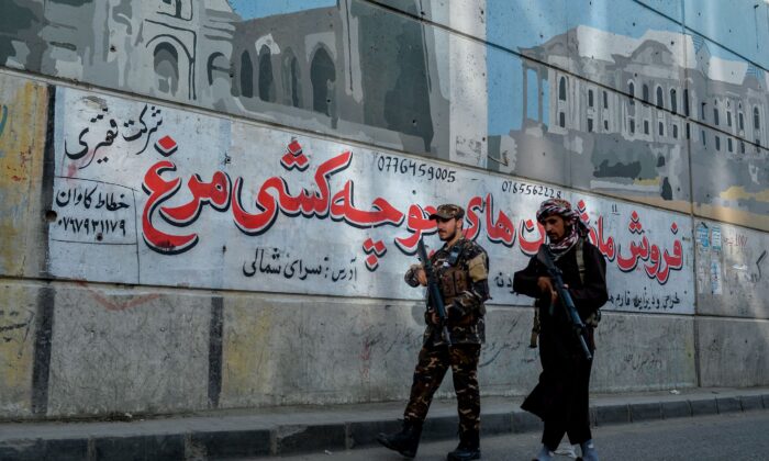 Talibanes patrullan a lo largo de una carretera con el telón de fondo de un mural pintado en la pared de un paso elevado en Kabul el 26 de septiembre de 2021. (Hoshang Hashimi/AFP vía Getty Images)