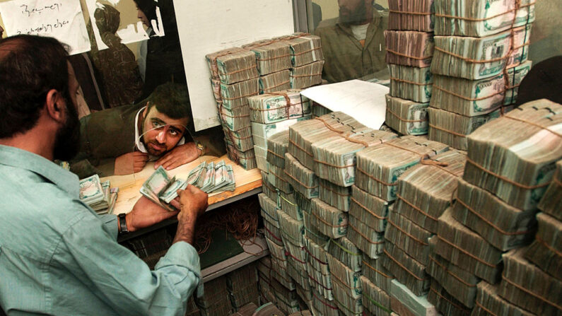 Un hombre afgano no identificado mira a un cajero de banco mientras cambia dinero antiguo afgano por nueva moneda en el Banco Central, el 9 de octubre de 2002, en Kabul, Afganistán. (Chris Hondros/Getty Images)