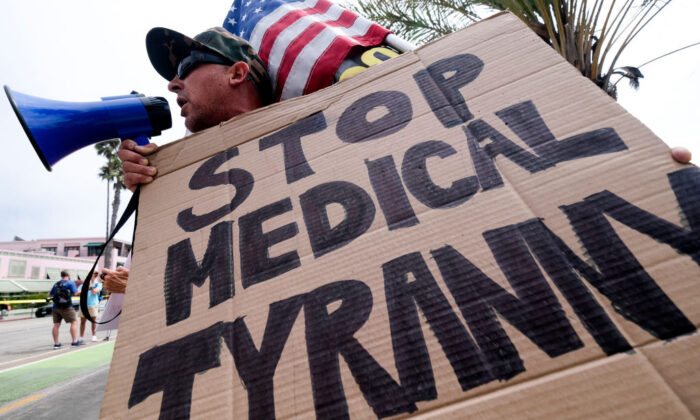 Un manifestante sostiene una pancarta y una bandera mientras participa en una concentración contra la orden de vacunación COVID-19, en Santa Mónica, California, el 29 de agosto de 2021. (Ringo Chiu/AFP vía Getty Images)