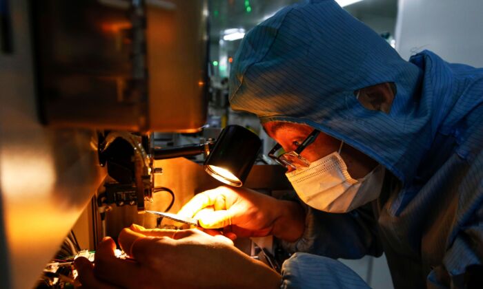 Un empleado chino con mascarilla y traje de protección trabaja en una línea de producción de chips inteligentes en el Condado de Sihong, en la provincia oriental china de Jiangsu, el 16 de febrero de 2020. (STR/AFP)