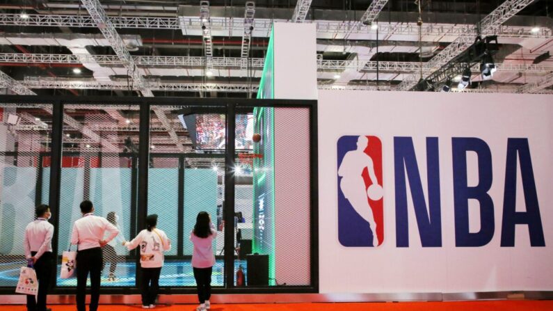 Un grupo de personas se encuentra junto a un logotipo de la NBA en la exposición de la NBA en la 3ª Exposición Internacional de Importación de China (CIIE), en Shanghai, China, el 5 de noviembre de 2020. (STR/AFP vía Getty Images)
