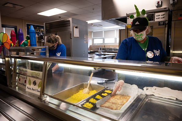 Trabajadores de cafetería portando mascarilla sirven la comida durante un almuerzo con medidas de distanciamiento social en la Escuela Primaria Medora el 17 de marzo de 2021 en Louisville, Kentucky. Hoy marca la reapertura de las escuelas públicas del condado de Jefferson para el aprendizaje en persona con los nuevos procedimientos COVID-19 en su lugar. (Foto de Jon Cherry/Getty Images)