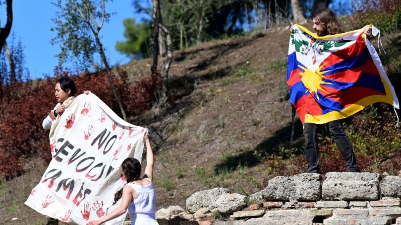 Tres manifestantes despliegan una pancarta y una bandera tibetana durante la ceremonia de encendido de la llama para los Juegos Olímpicos de Invierno de Beijing 2022 en el sitio arqueológico de la Antigua Olimpia, cuna de los antiguos Juegos Olímpicos en el sur de Grecia, el 18 de octubre de 2021.(ARIS MESSINIS/AFP vía Getty Images)