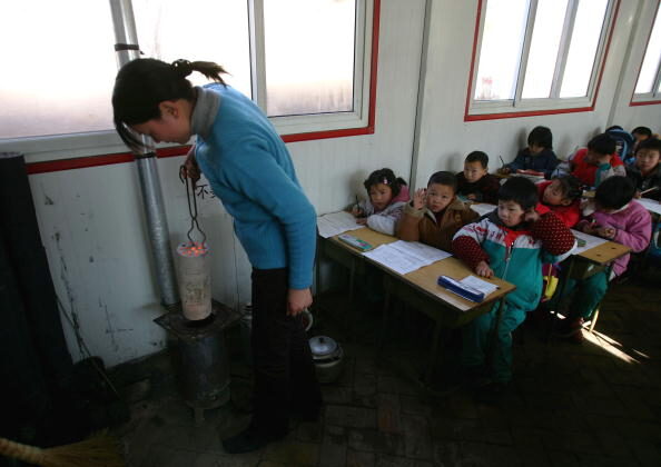 Una maestra prepara una estufa para calentar un aula de la Escuela Primaria Xingzhi, una de las mayores escuelas de niños inmigrantes de Beijing (China), el 28 de diciembre de 2004. (Cancan Chu/Getty Images)