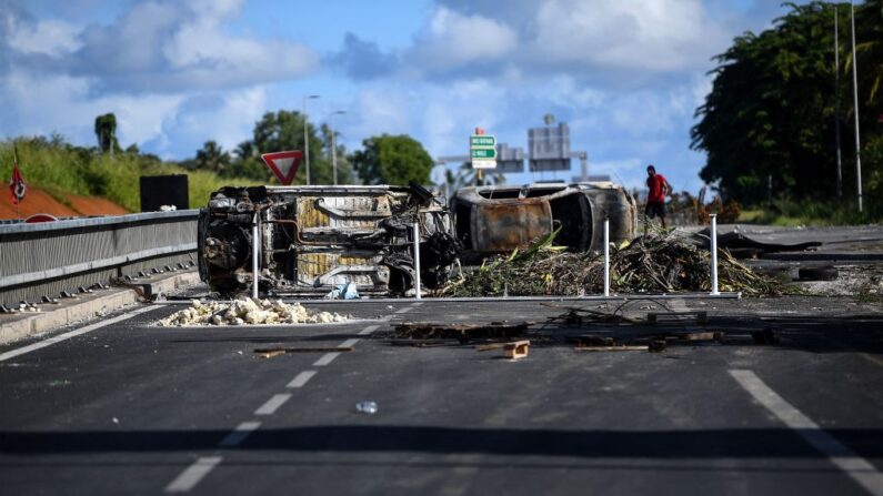 Un manifestante pasa por delante de vehículos quemados tirados en una carretera como parte de un bloqueo en la rotonda de Perrin en Les Abymes, cerca de Pointe-a-Pitre en la isla caribeña francesa de Guadalupe, el 22 de noviembre de 2021. (Foto de CHRISTOPHE ARCHAMBAULT/AFP a través de Getty Images)
