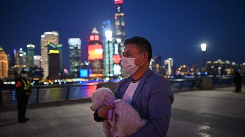 Un hombre con una mascarilla en medio de la preocupación por el brote de COVID-19 camina sosteniendo a su perro a lo largo del paseo del Bund junto al río Huangpu en Shanghai, China, el 20 de marzo de 2020. (Hector Retamal/AFP vía Getty Images)