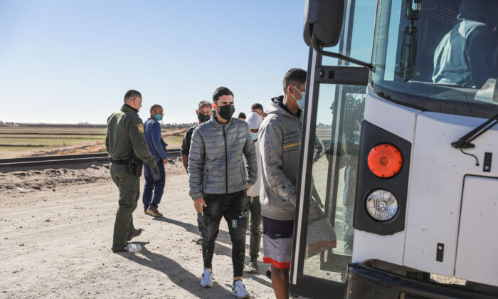 Inmigrantes ilegales reunidos junto al muro fronterizoentre Estados Unidos y México suben a un autobús que se dirige a la estación de la Patrulla Fronteriza para su procesamiento en Yuma, Arizona, el 10 de diciembre de 2021. (Charlotte Cuthbertson/The Epoch Times)