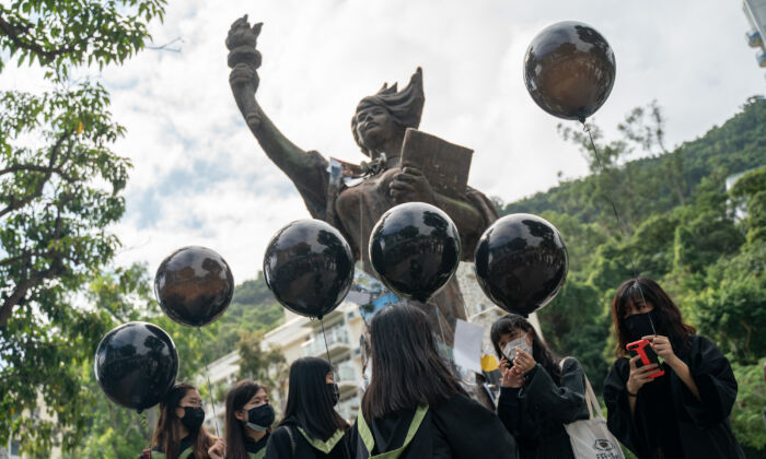 Estudiantes con togas y mascarillas negras se paran frente a la estatua de la Diosa de la Democracia, en el campus de la Universidad China de Hong Kong, mientras sostienen globos negros, en Hong Kong, China, el 19 de noviembre de 2020. (Anthony Kwan/Getty Images)
