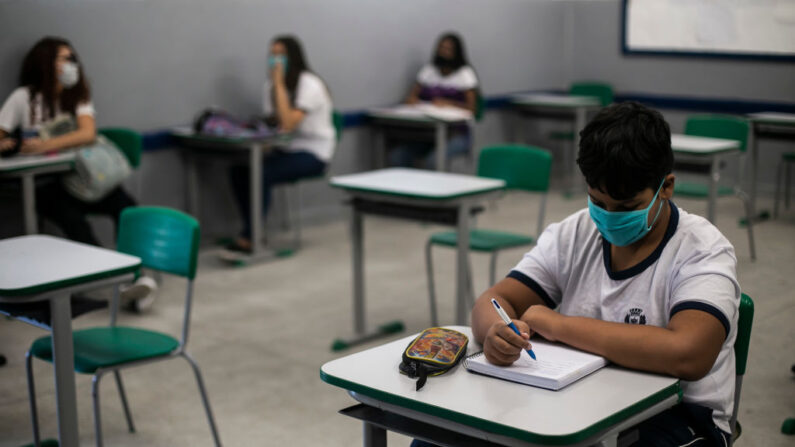 Un estudiante con mascarilla escribe en su cuaderno durante una clase en la Escuela Municipal de Aplicación Carioca Coelho, en el barrio Ricardo de Albuquerque el 24 de noviembre de 2020 en Río de Janeiro, Brasil. (Bruna Prado/Getty Images)