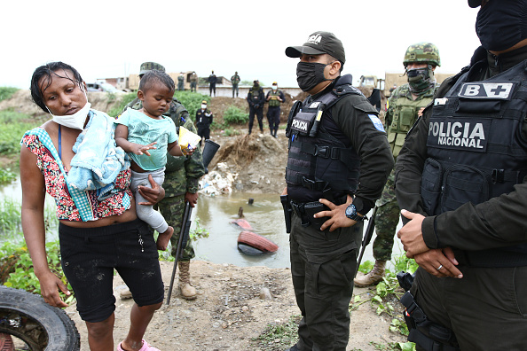 Una madre migrante venezolana sostiene a su hijo mientras intentan cruzar el Canal de Aguas Verdes hacia Perú, el 29 de enero de 2021, en Cantón Huaquillas, Ecuador. El Ejército peruano desplegó en la última semana 50 vehículos blindados para patrullar la frontera peruano-ecuatoriana del río Zarumilla y evitar que los migrantes venezolanos ingresen al país en medio de la oleada de COVID-19. (Foto de Gerardo Menoscal/Getty Images)