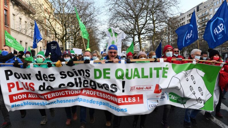 Trabajadores del sector sanitario sostienen una pancarta en la que se lee "¡Por una atención de calidad, más compañeros! No a las prohibiciones profesionales" mientras participan en una manifestación sindical contra la vacunación obligatoria contra el covid-19 en Bruselas (Bélgica) el 7 de diciembre de 2021. (John Thys/AFP vía Getty Images)