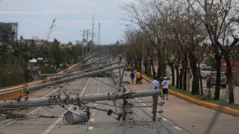 Los residentes caminan junto a los postes eléctricos derribados en la ciudad de Talisay, provincia de Cebú (Filipinas), el 17 de diciembre de 2021, un día después de que el tifón Rai azotara las regiones del sur y el centro de Filipinas. (Alan Tangcawan/AFP vía Getty Images)