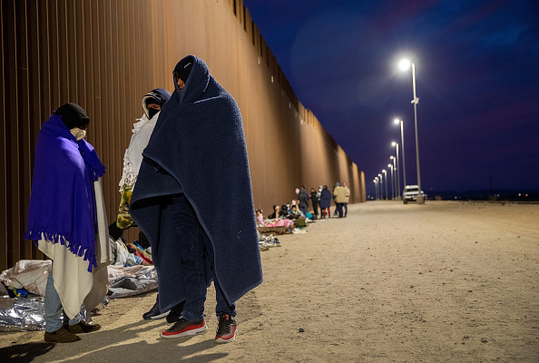 Padres cubanos esperan junto al muro fronterizo entre Estados Unidos y México antes de ser detenidos por agentes de la Patrulla Fronteriza de Estados Unidos el 07 de diciembre de 2021 en Yuma, Arizona. Habían cruzado desde México con sus familias en días anteriores para pedir asilo político en Estados Unidos. Las instalaciones de detención de la Patrulla Fronteriza en Yuma estaban desbordadas con miles de recién llegados, con muchas familias que intentaban llegar a suelo estadounidense antes de la reimplantación ordenada por la corte de la política de Permanecer en México de la era Trump. (Foto de John Moore/Getty Images)