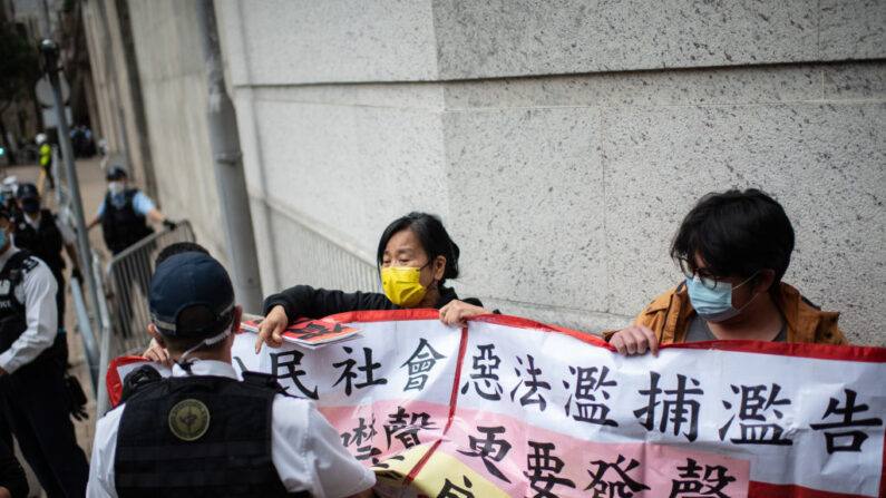 La policía monta guardia mientras integrantes de la Liga de Socialdemócratas realizan una protesta de tres personas frente al colegio electoral donde la directora ejecutiva de Hong Kong da su voto en las elecciones al Consejo Legislativo, el 19 de diciembre de 2021, en Hong Kong. (Louise Delmotte/Getty Images)