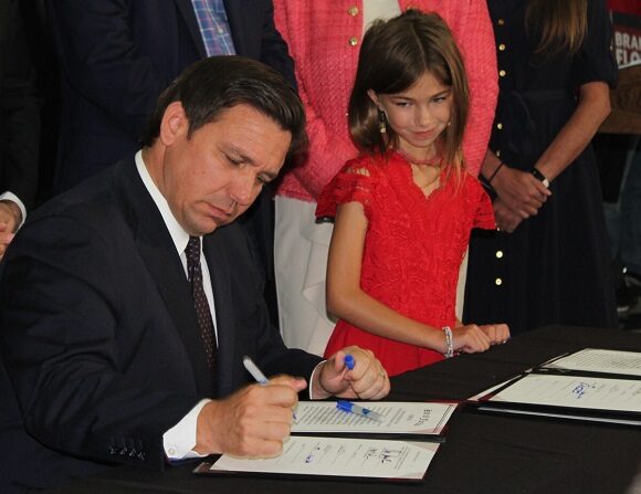 El gobernador de Florida, Ron DeSantis, firma los proyectos de ley con la niña de segundo grado Fiona LaShells mirando. 18 de noviembre de 2021 (Jann Falkenstern, The Epoch Times)