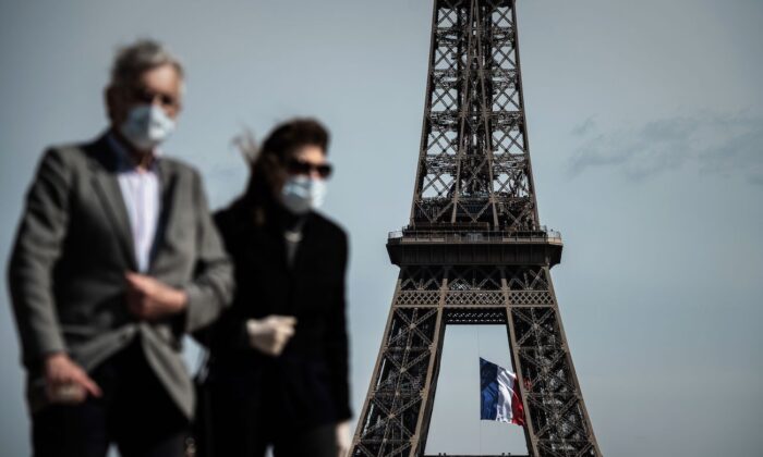 Un hombre y una mujer con mascarillas caminan en Trocadero Plaza mientras una bandera nacional francesa ondea en la Torre Eiffel de fondo en París, el 11 de mayo de 2020. (Philippe Lopez/AFP vía Getty Images)