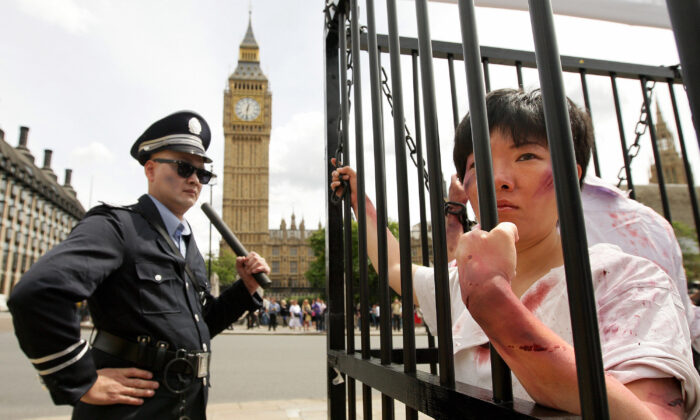 Un actor disfrazado de policía chino (izq.) vigila una jaula con actores disfrazados de practicantes de Falun Gong, durante una manifestación ante el Parlamento de Londres, el 20 de julio de 2009. (Shaun Curry/AFP vía Getty Images)
