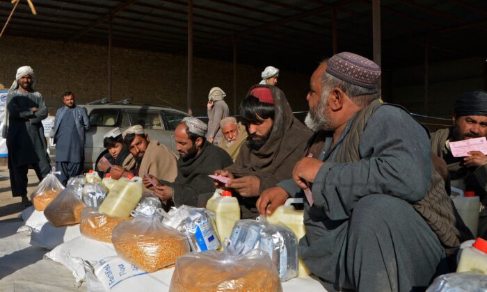 Hombres afganos sentados junto a los paquetes de alimentos que distribuyen los miembros del Programa Mundial de Alimentos (PMA) a las familias necesitadas en Kandahar (Afganistán) el 23 de diciembre de 2021. (Javed Tanveer/AFP vía Getty Images)