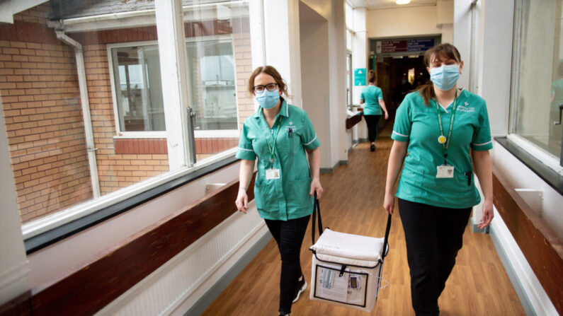 Empleados transportan una nevera que contiene la vacuna de Moderna contra el COVID-19 en el Hospital General de Gales Occidental en Carmarthen, Gales, el 7 de abril de 2021. (Jacob King/Pool/AFP vía Getty Images)