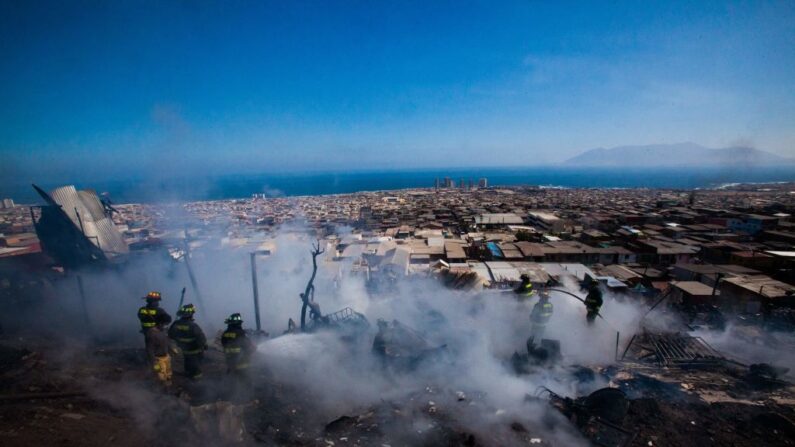 En una foto de archivo, los bomberos trabajan para apagar un incendio que afectó a decenas de casas de material ligero en dos campamentos de migrantes en Antofagasta, Chile, el 13 de mayo de 2021. (Glenn Arcos/AFP vía Getty Images)