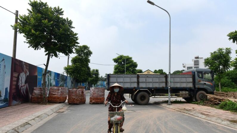 Una residente local pasa con su bicicleta por delante de una barricada improvisada con pilas de ladrillos y un camión aparcado para impedir los desplazamientos no autorizados en un barrio de Hanoi el 30 de julio de 2021. (NHAC NGUYEN/AFP vía Getty Images)