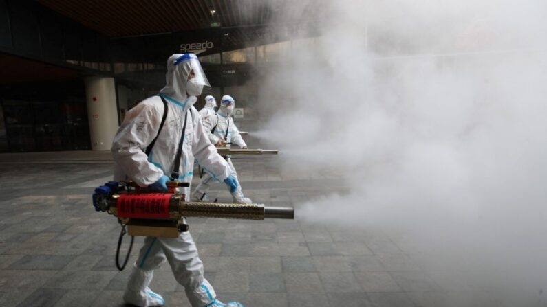 Miembros del personal con equipo de protección personal (EPP) rocían desinfectante fuera de un centro comercial en Xi'an, China, el 11 de enero de 2022. (STR/AFP vía Getty Images)