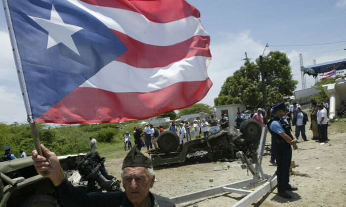 Bernardo Rivera celebra sosteniendo una bandera puertorriqueña mientras camina alrededor de un vehículo militar quemado en la antigua estación naval estadounidense Campamento García en Vieques, Puerto Rico, el 1 de mayo de 2003.  (Gerald Lopez-Cepero/Getty Images)