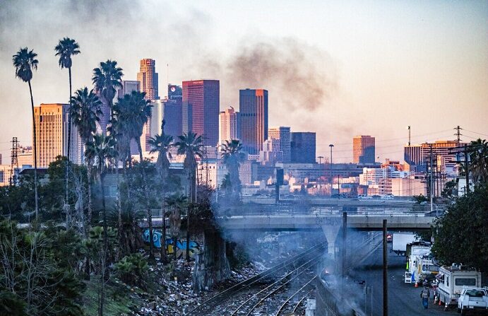 Un incendio arde en un campamento de indigentes mientras cajas destrozadas cubren las vías del tren en Los Ángeles, California, el 20 de enero de 2022. (John Fredricks/The Epoch Times)