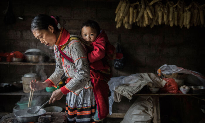 Una mujer lleva a un bebé a la espalda mientras cocina en la aldea de Xiaobatian, provincia de Guizhou, sur de China, el 7 de febrero de 2017. (Kevin Frayer/Getty Images)
