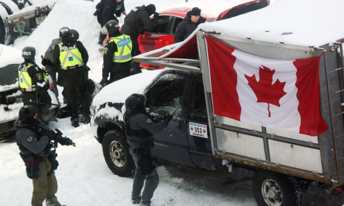 Un agente de policía se acerca y rompe las ventanas a un camión mientras las fuerzas de seguridad se despliegan para desalojar a los manifestantes en Ottawa el 19 de febrero de 2022. (Dave Chan/AFP vía Getty Images)