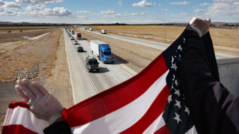 Los simpatizantes sostienen una bandera estadounidense mientras observan desde un paso elevado al "Convoy del Pueblo" en su camino a Washington, DC para protestar contra los mandatos relacionados con el COVID-19 el 23 de febrero de 2022 cerca de Barstow, California. (Mario Tama/Getty Images)